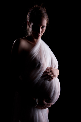 Schwanger in Düsseldorf. Die Göttin. Wunderschöne Schwangere steht einer Göttin gleich mit weichem weißen Tuch umhüllt und schaut in die Kamera.
